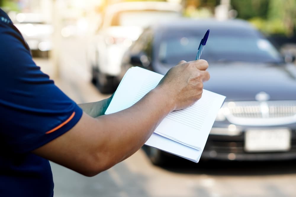 A car insurance agent writes details about a car damaged from an accident on paper. Blurred car background.